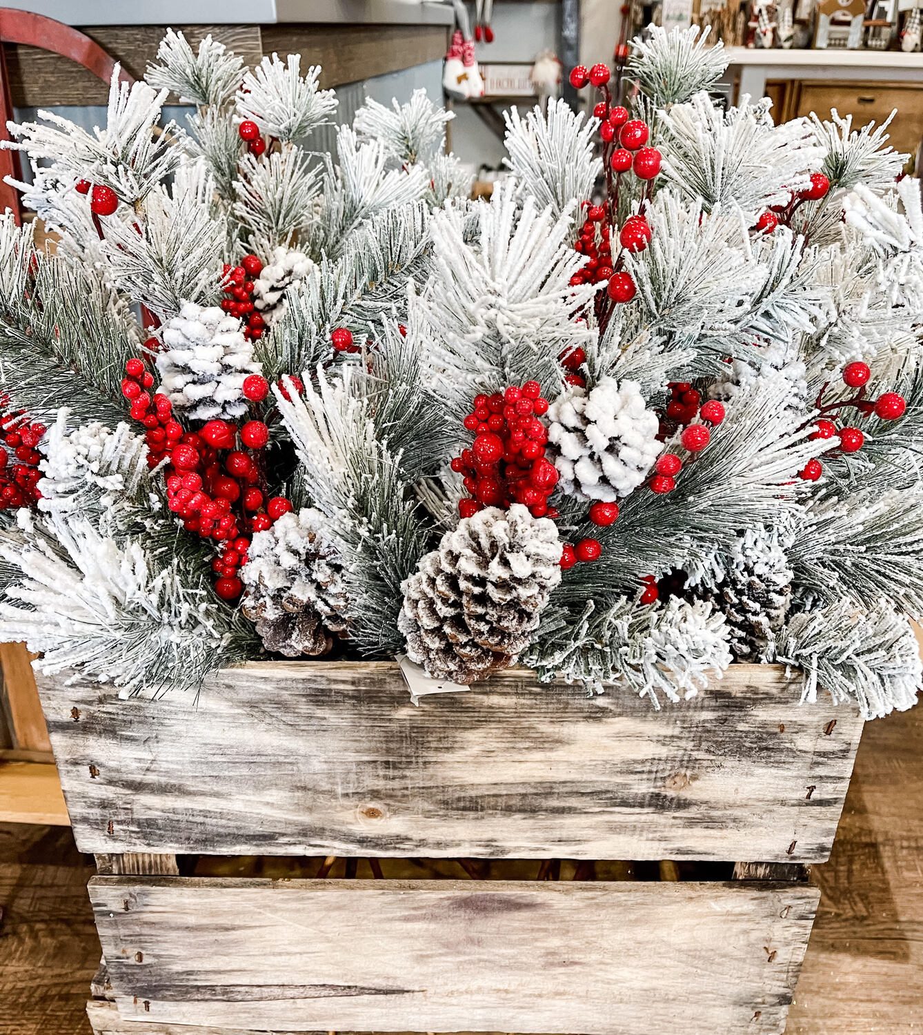 Flocked porch pot with red berries and pinecones in a whitewashed wooden crate